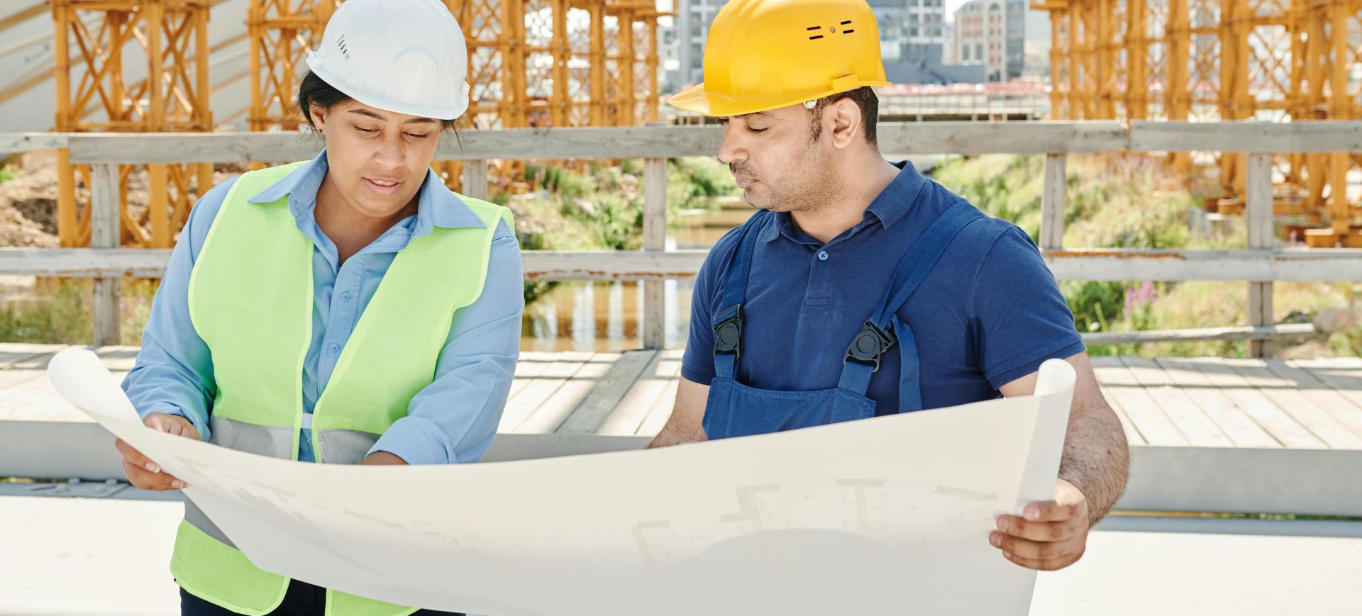 Engineering team analyzing blueprints together at an outdoor construction site with safety gear.